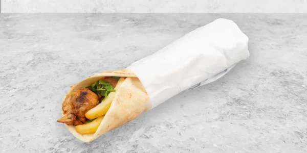 A chicken shawarma wrap with fries and greens, partially wrapped in white paper, placed on a gray stone surface—a delicious alternative to a Fried Shrimp Sandwich.